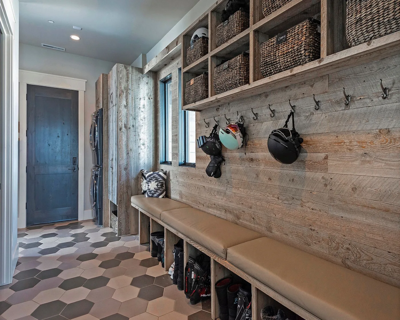 Mudroom with horizontal wood walls, long cushioned bench, helmet hooks, upper woven baskets, lower boot spaces and patterned hexagonal floor