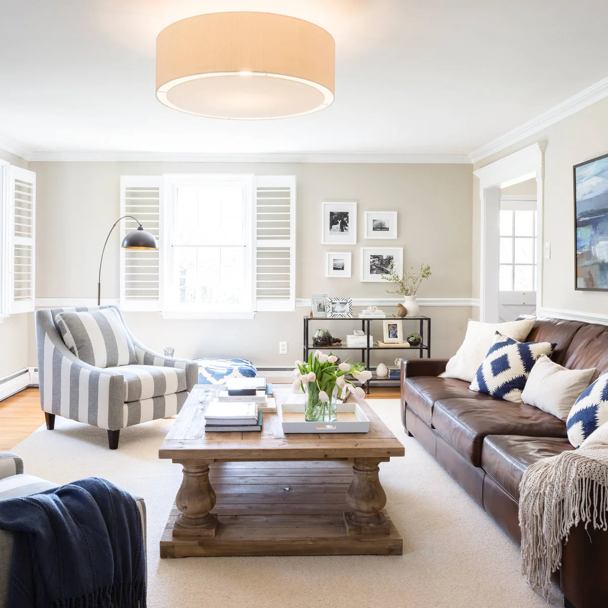 A brown leather sofa faces a striped armchair across a wood coffee table, with another pale chair in the foreground.
