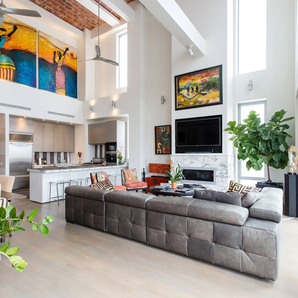 Colorful framed painting above a television beside tall windows in a bright room with an open white ceiling.