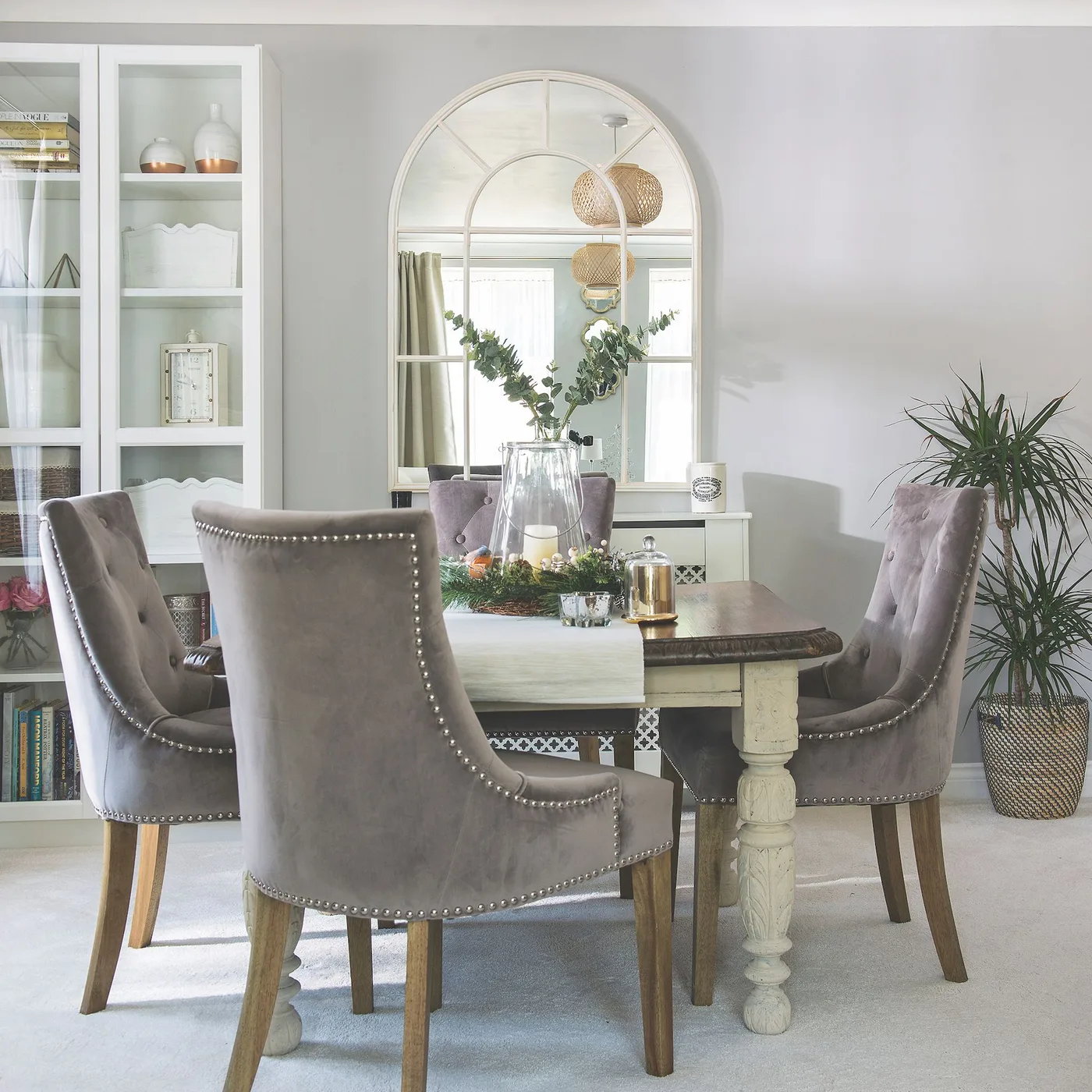 Pale arched grid mirror beside a glazed cabinet behind a dining table with gray upholstered chairs