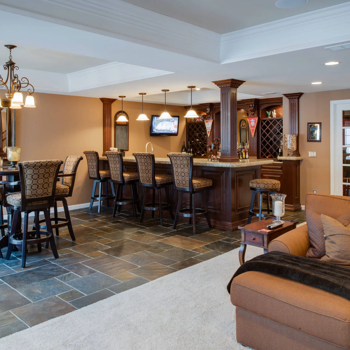 Traditional basement bar with patterned stools and a nearby tall table with matching seats
