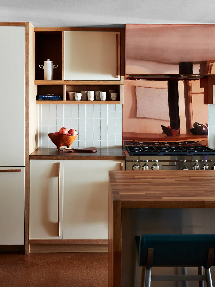 Cream cabinet doors sit within timber frames beside open shelves and a copper-colored backsplash