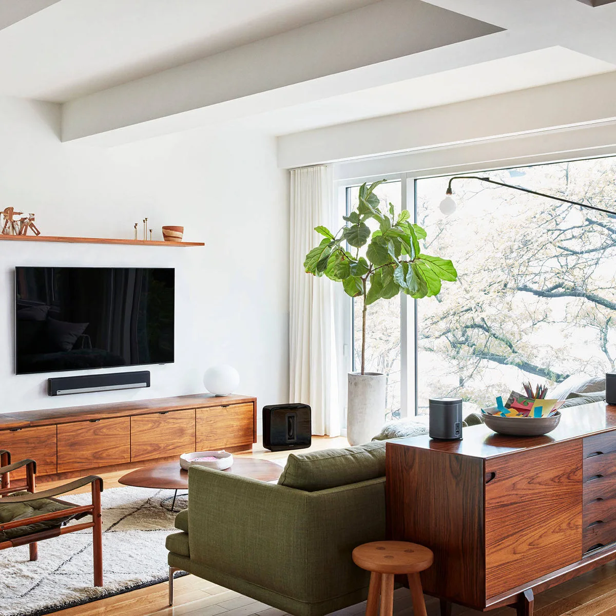 A long wood cabinet beneath a television and soundbar holds one small white vessel near its end.