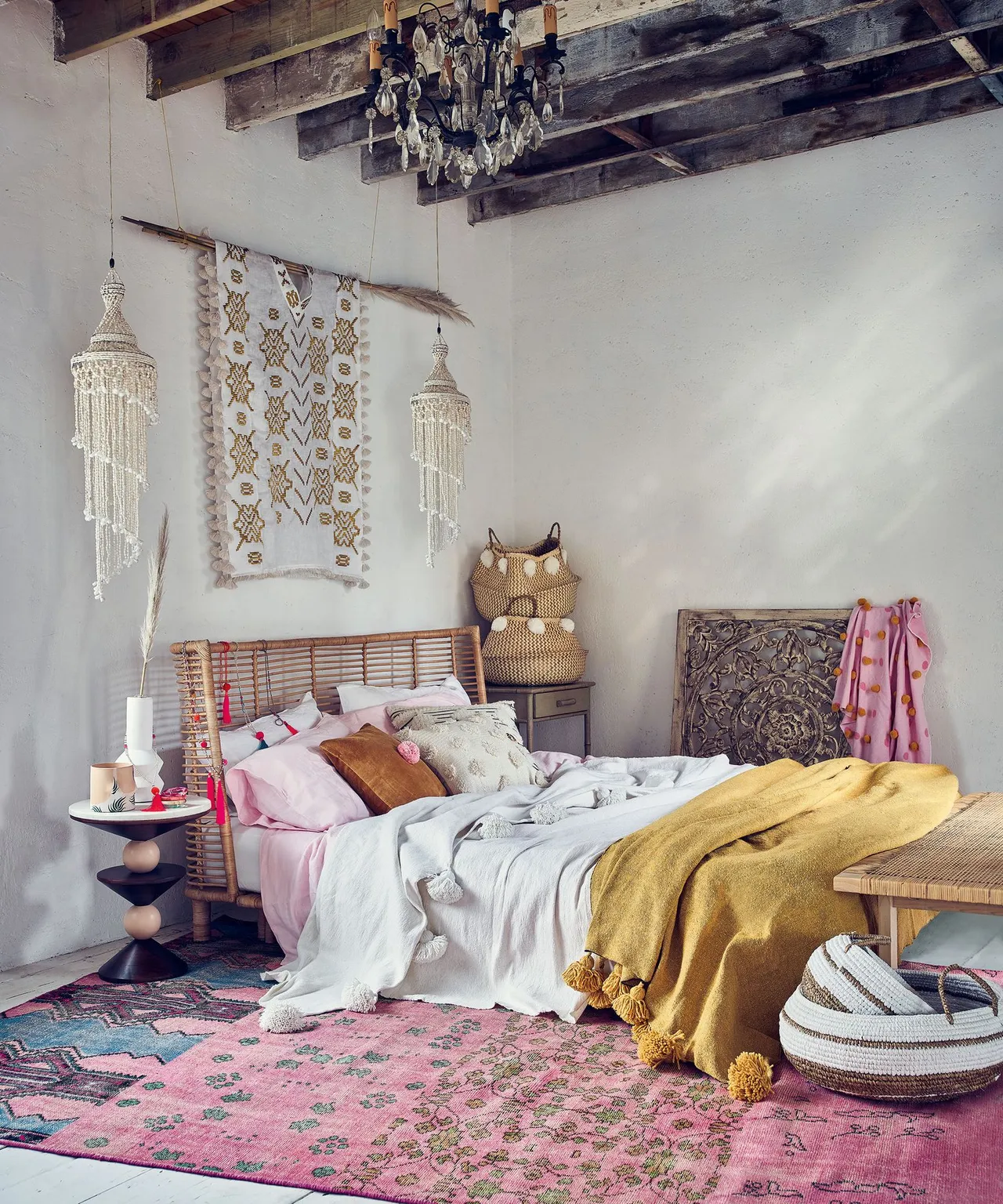 A mustard blanket lies across pale bedding beneath woven wall decorations.