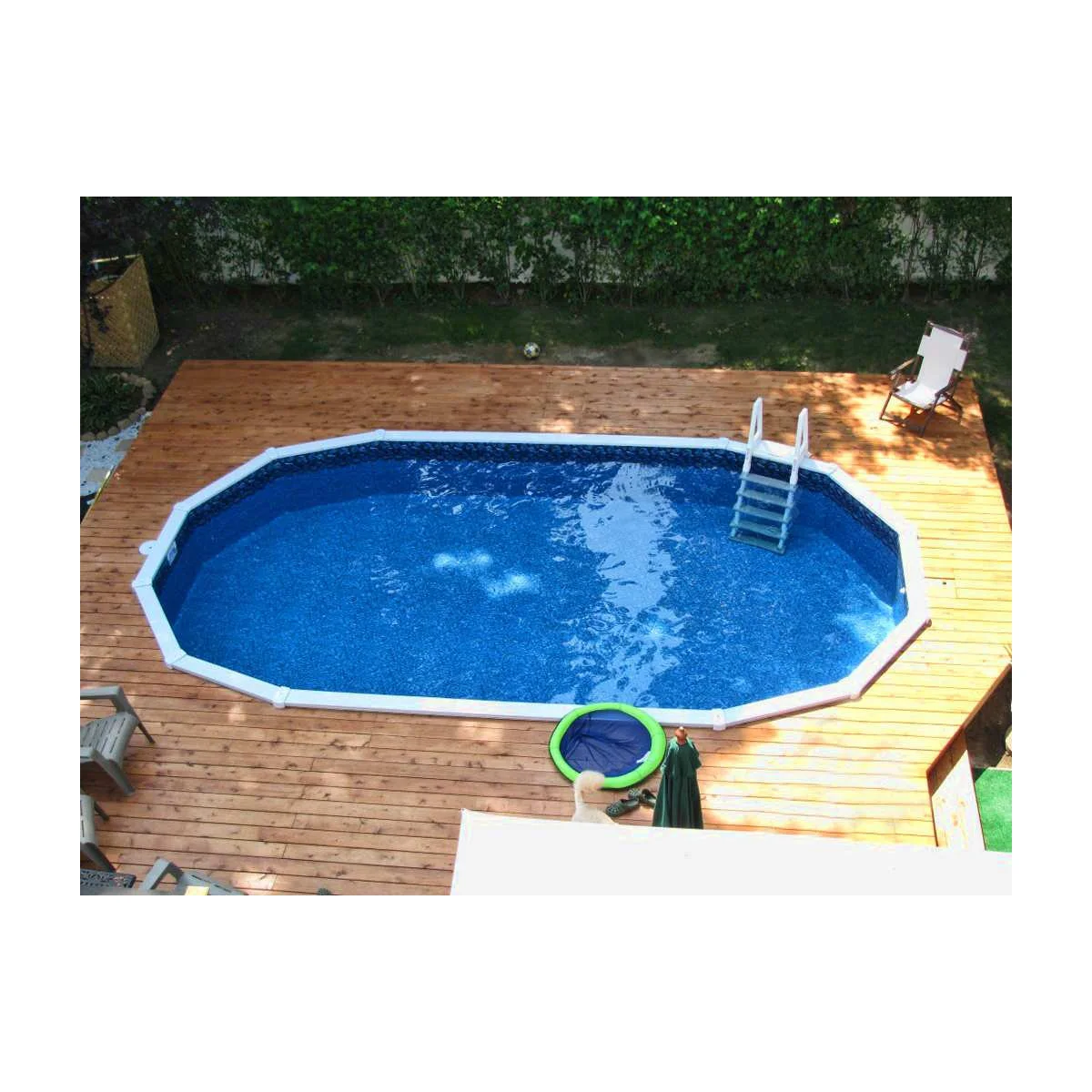 Oval above-ground pool within a wood deck with an entry ladder, one pale chair and limited furniture near the edge.