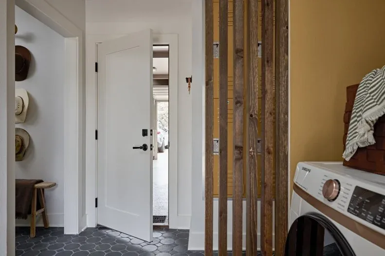 Open white doorway beside a wooden slat divider with laundry appliances and dark rounded floor tiles.