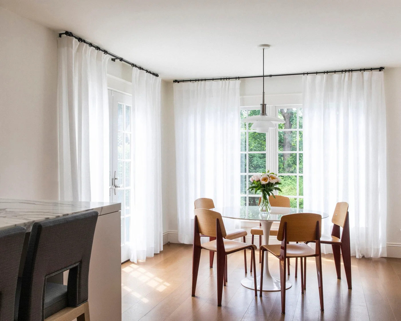 White sheer curtains around corner glazing beside a round kitchen dining table
