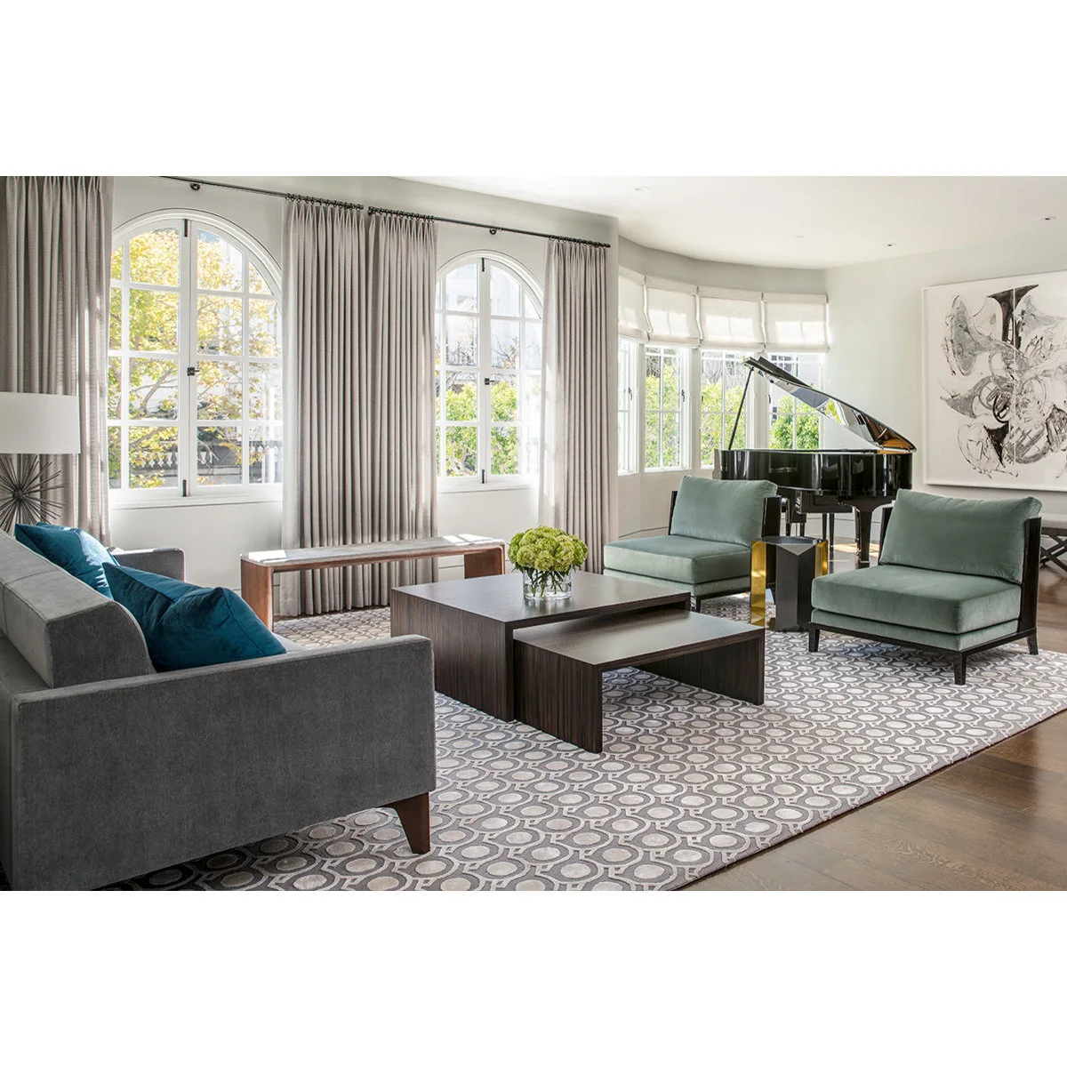 Gray sofa and two green chairs around dark nesting tables with a grand piano in the window bay beyond