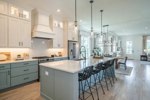 Pale blue lower cabinets and an island sit beneath white cabinetry beside an open dining area.