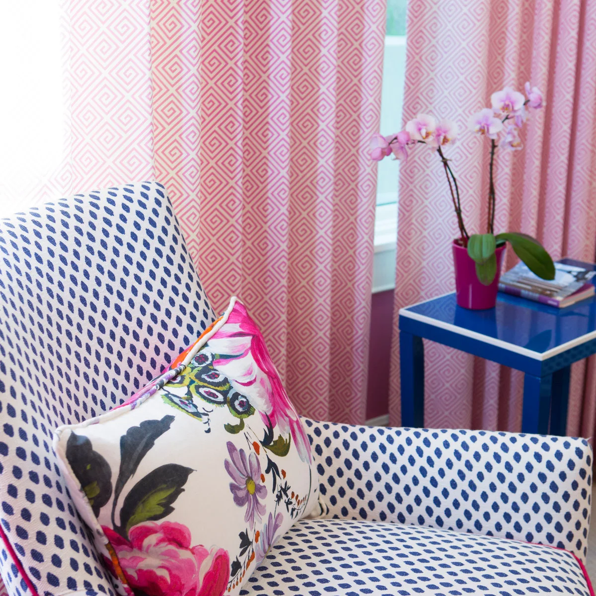 Blue-and-white patterned chair beside pink geometric curtains and a small blue table