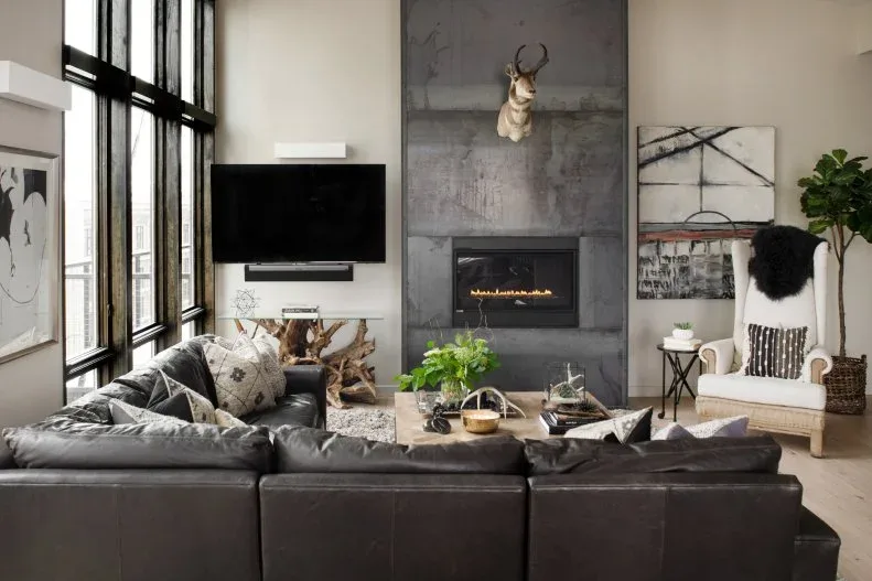 Tall gray fireplace wall with decorative animal head, television on adjacent white section and dark sectional