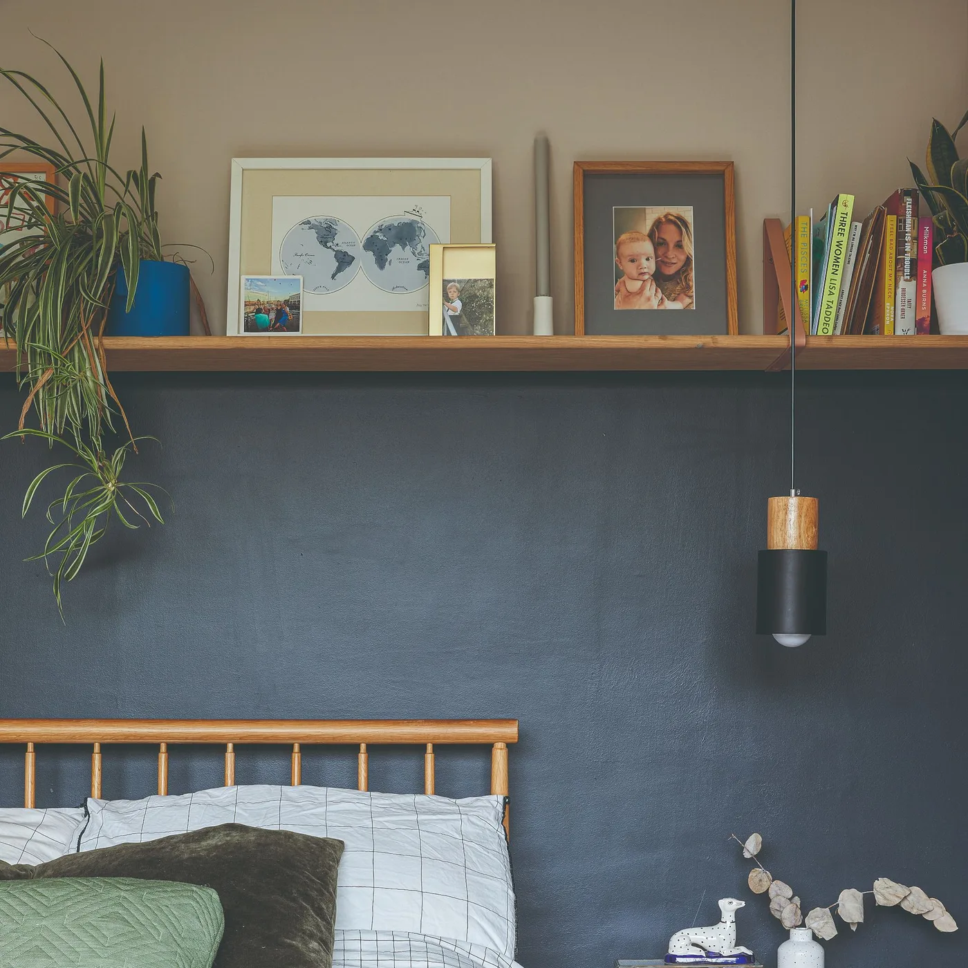Navy lower bedroom wall beneath a long wooden shelf with books and pictures, pale upper walls, and a dark hanging light.