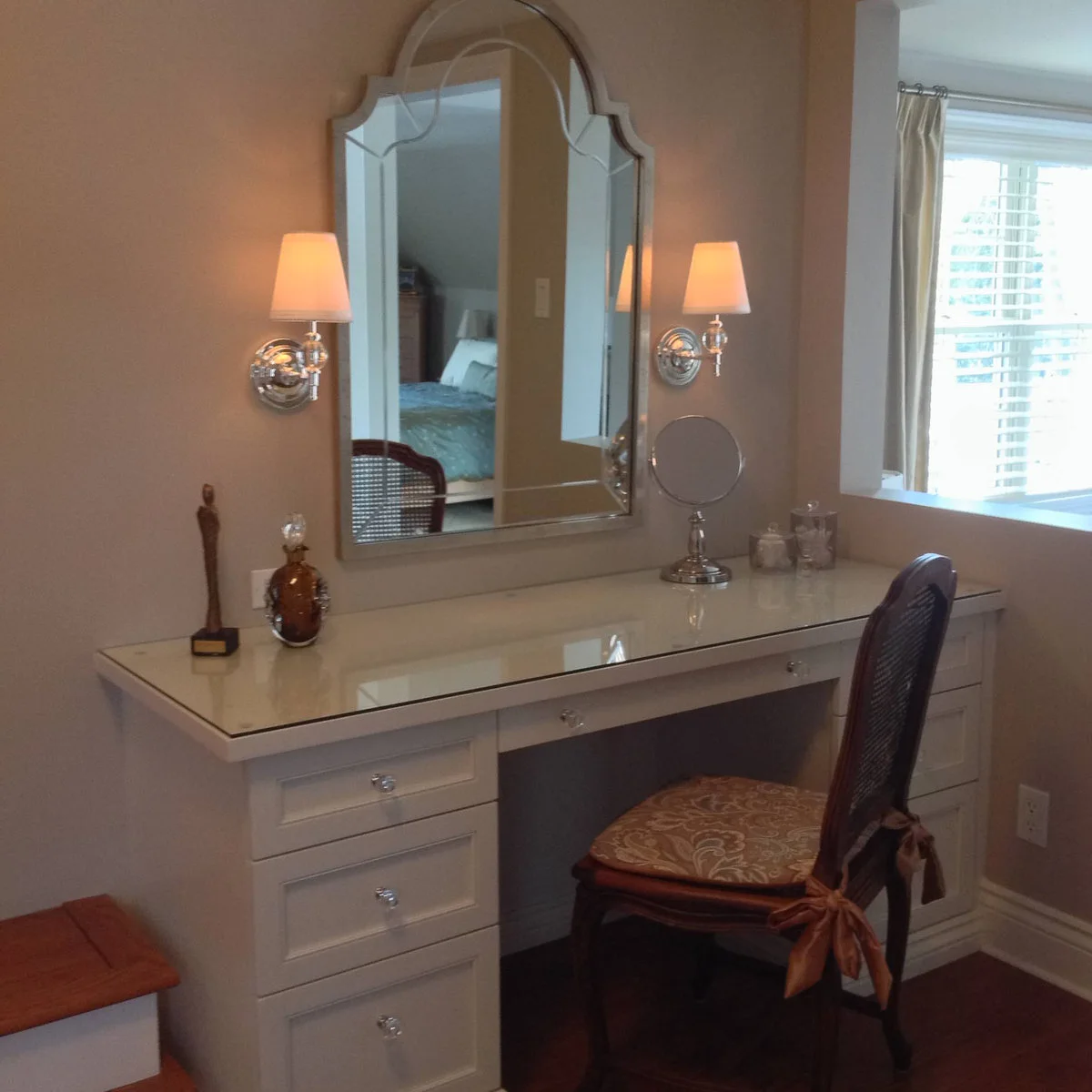 A pale dressing table with a tall shaped mirror has matching shaded wall lights on either side