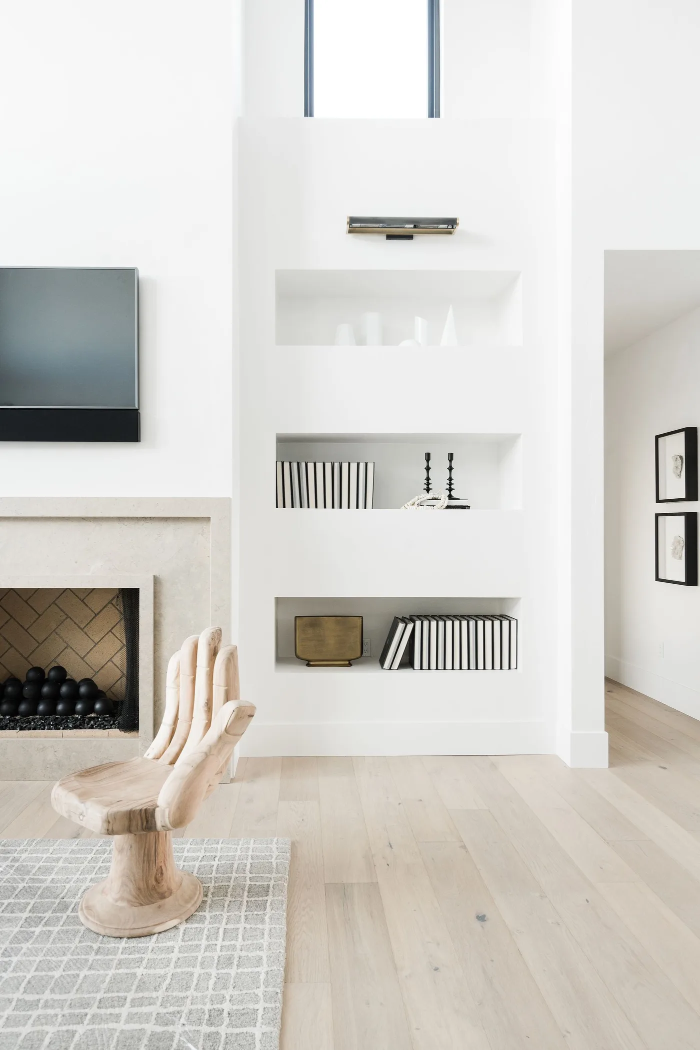 Carved hand-shaped wood chair beside a pale fireplace wall, built-in shelves and a light wood floor