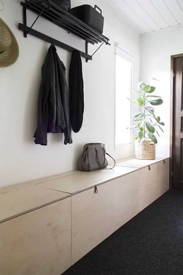 Narrow entrance with low wood storage cabinets, a black coat rack and a small window