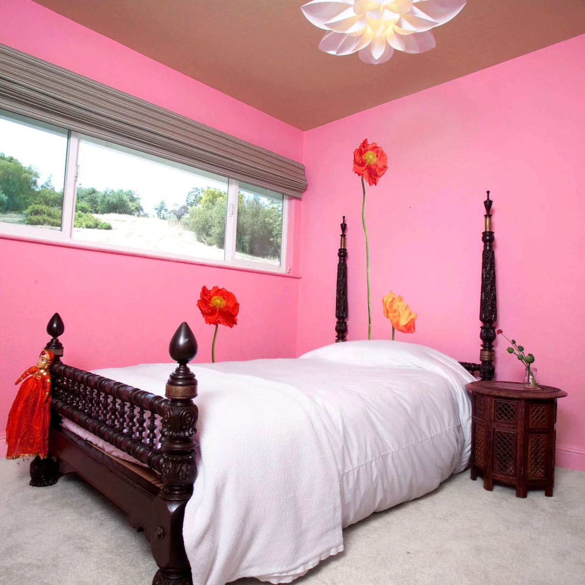 Bright pink bedroom with dark carved bed, plain white bedding and tall flower decorations