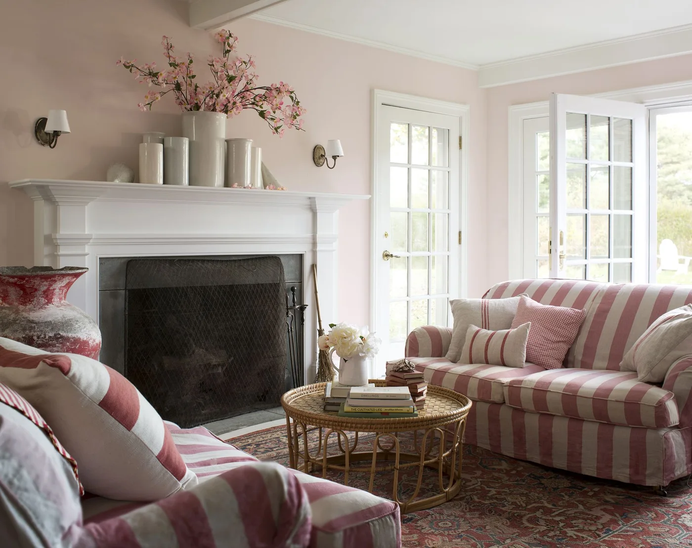A white molded fireplace stands against pink walls between pink-and-white striped sofas, with a dark screen across the opening.