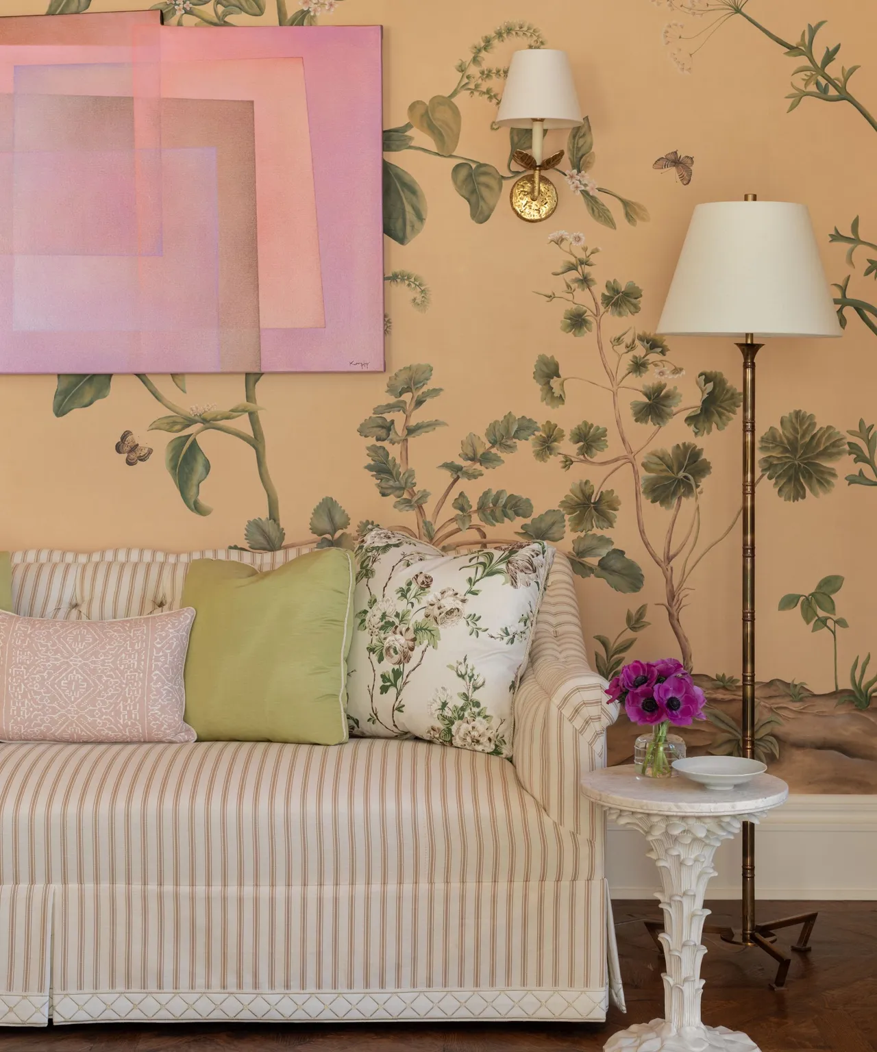 A light striped sofa sits beneath pink artwork against a warm floral wall