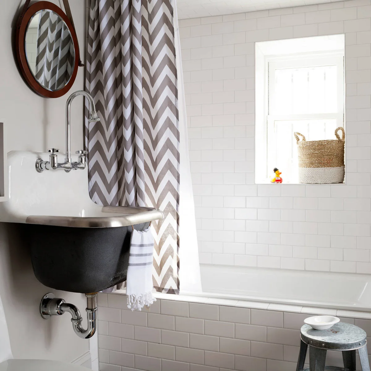 A gray-and-white chevron shower curtain hangs beside a white tiled bath and a dark wall-mounted sink.