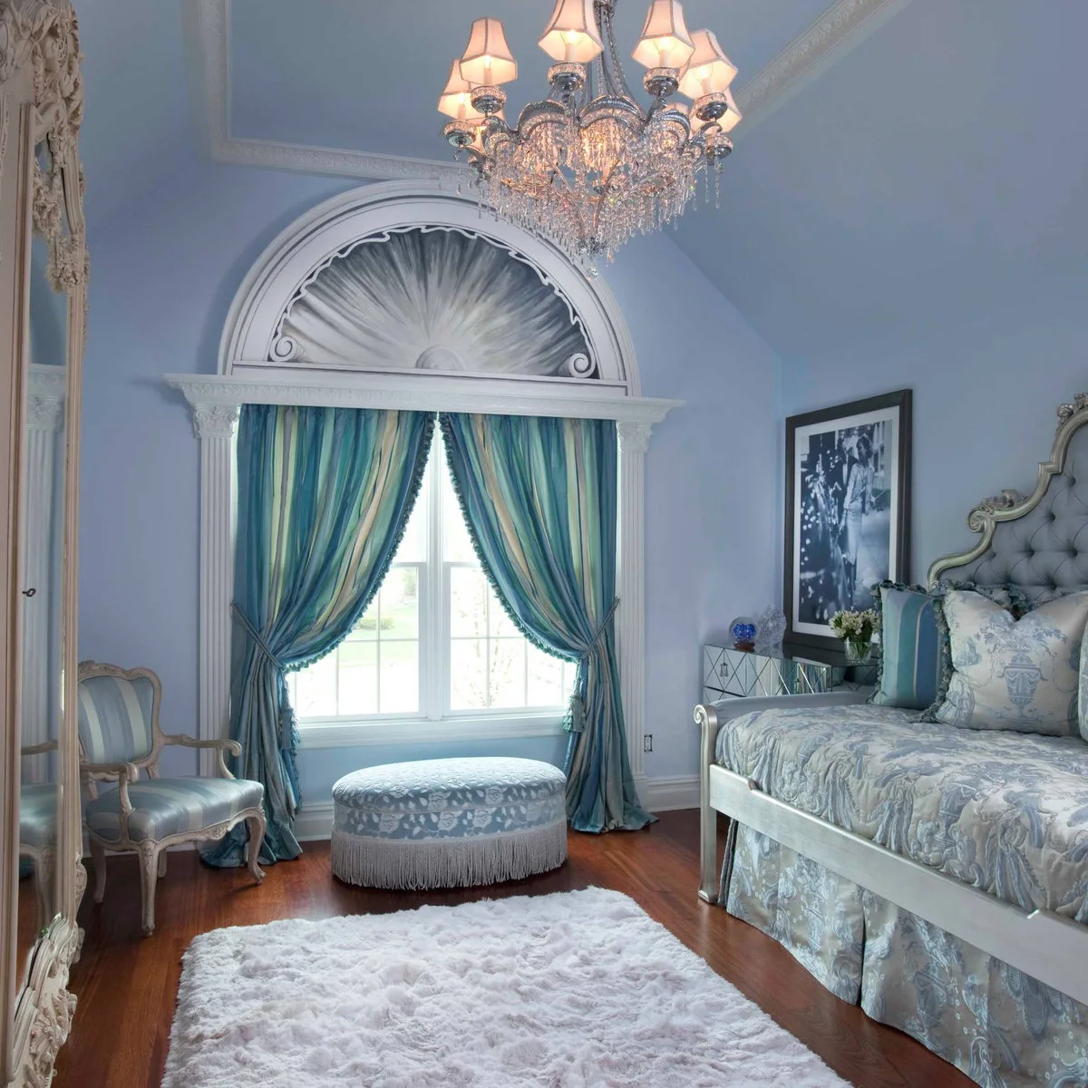 Ornate bedroom with pale blue walls and ceiling, blue-green curtains, a patterned daybed and chandelier