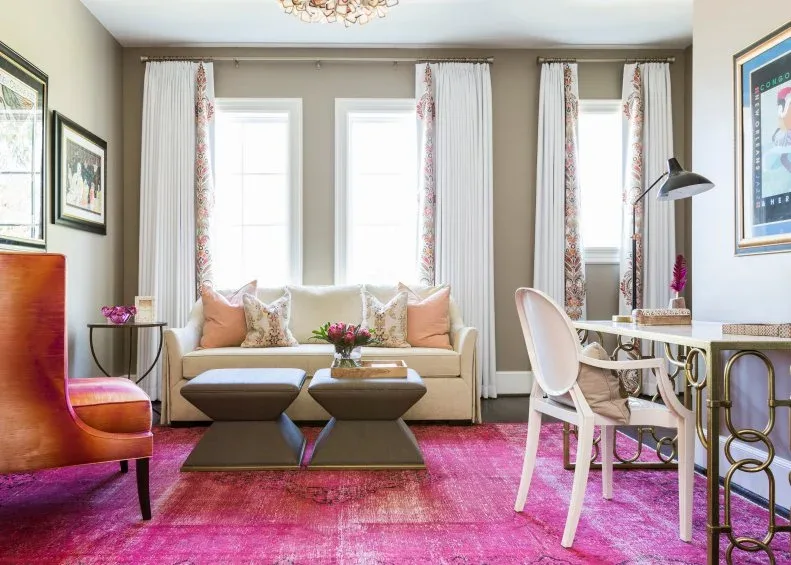 Office sitting area with a vivid pink rug, pale sofa and a desk with gold-toned loop-shaped supports.