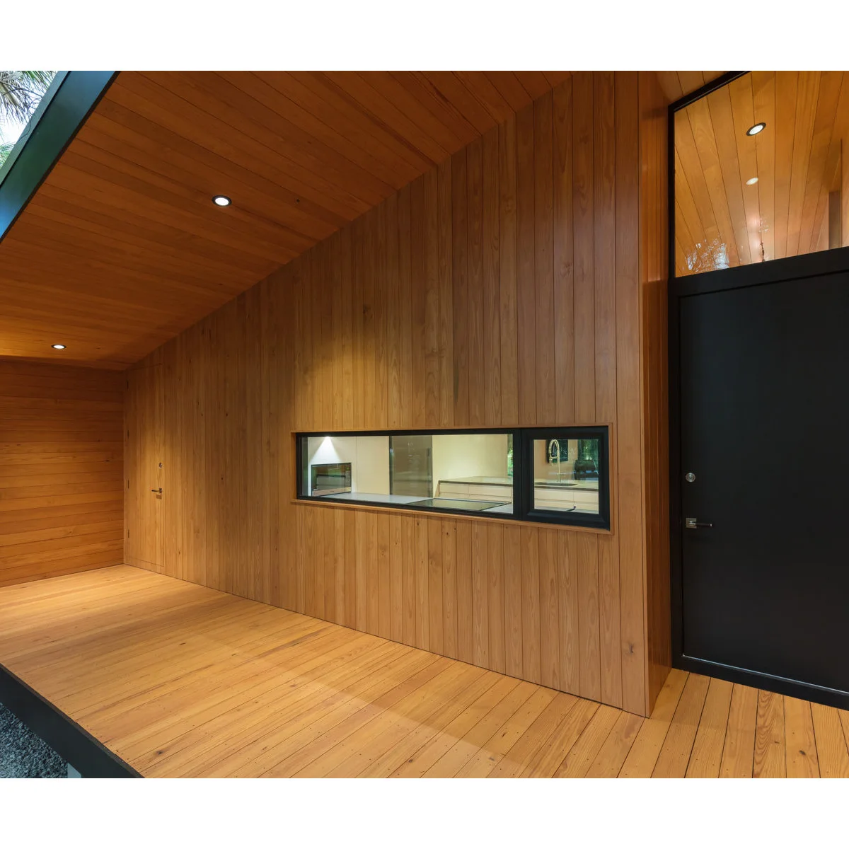 Small wood-lined entrance alcove with a dark door, horizontal window and recessed ceiling lights