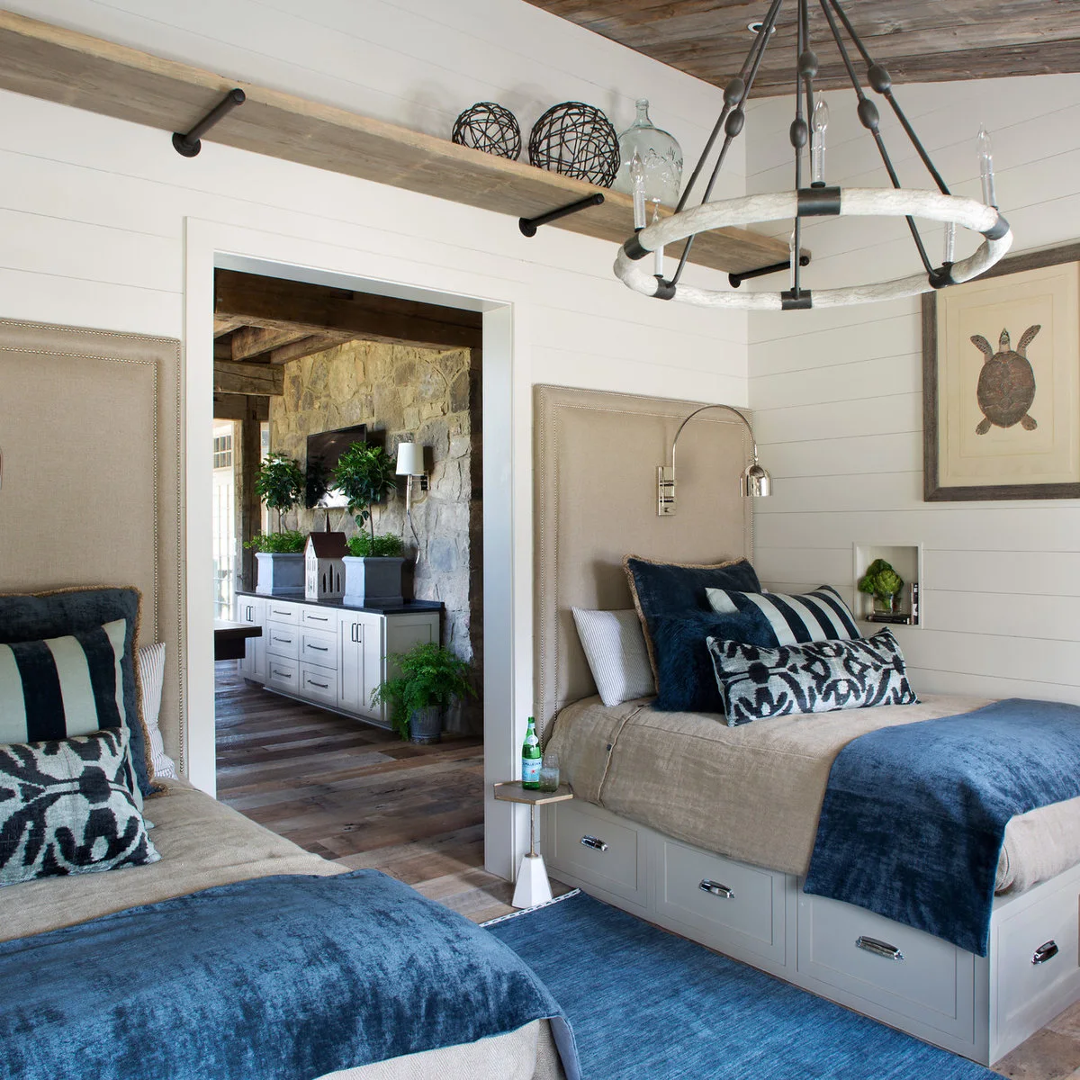 Two beds with white drawer bases, tall neutral headboards, blue throws and small bedside shelves