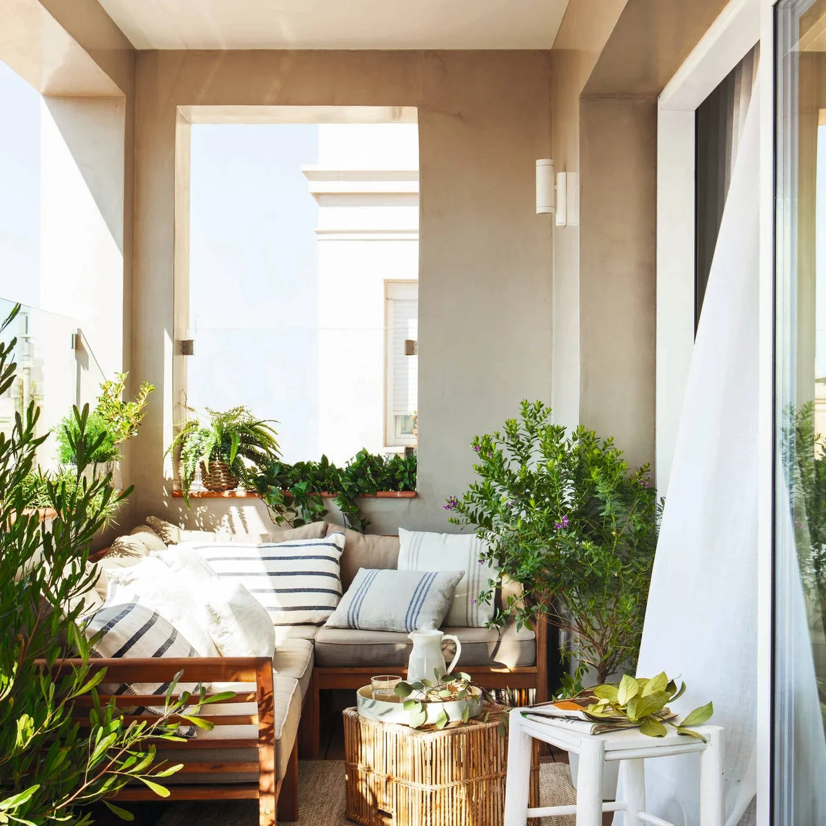 Planted apartment balcony with wood-framed corner seating, striped cushions and small tables