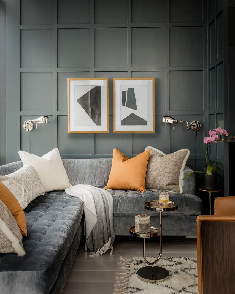 Two small framed prints sit above a gray sectional on a dark paneled wall