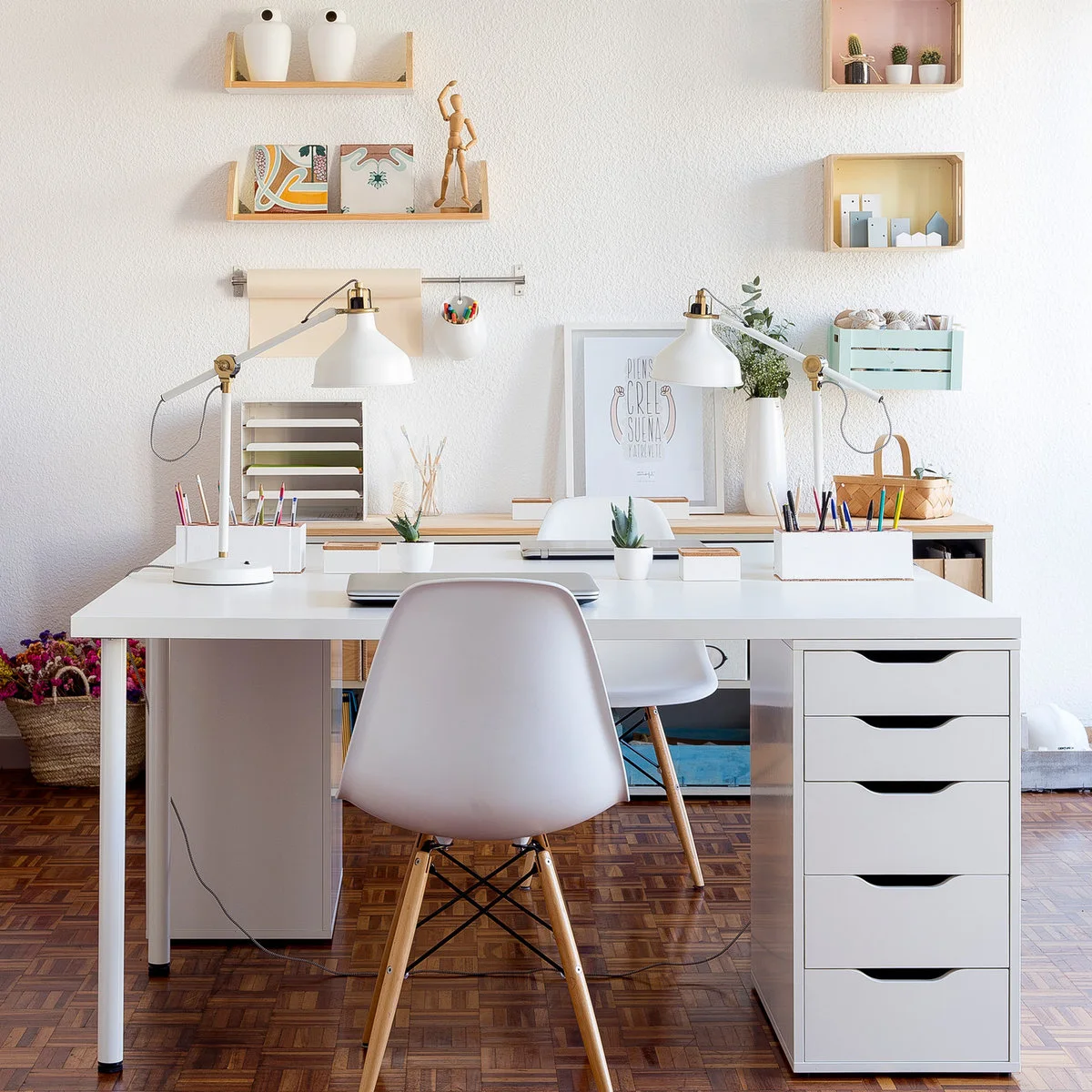 Two pale desks facing one another with white chairs, adjustable lamps and a white drawer unit
