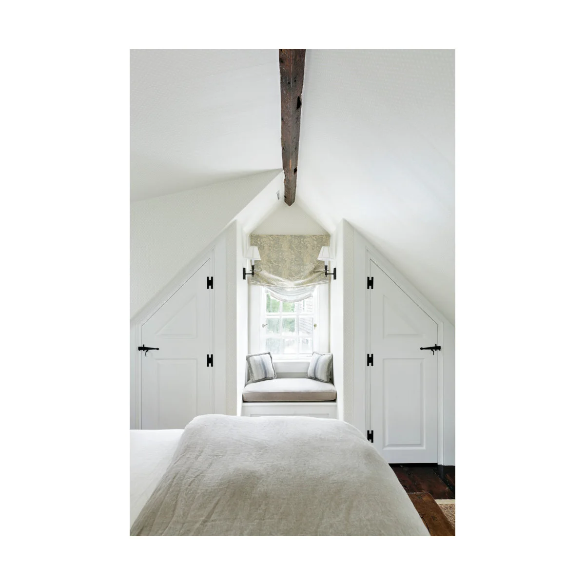 Pale attic bedroom with sloping cupboards and a cushioned seat beneath the end window