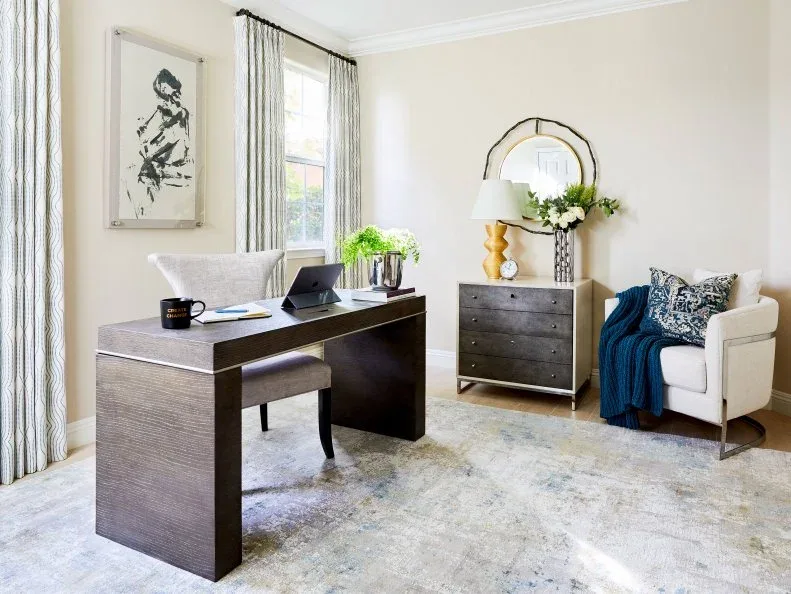 Dark office desk with a pale chair, a round layered mirror and a small chest beside a white armchair.