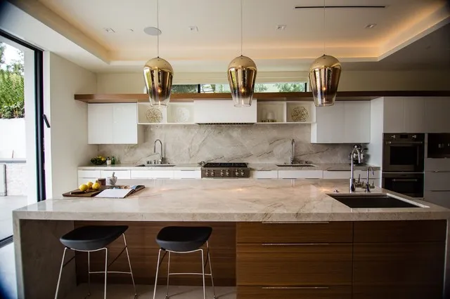 Black stools face a timber island with a pale counter below white upper cupboards and a narrow wood band