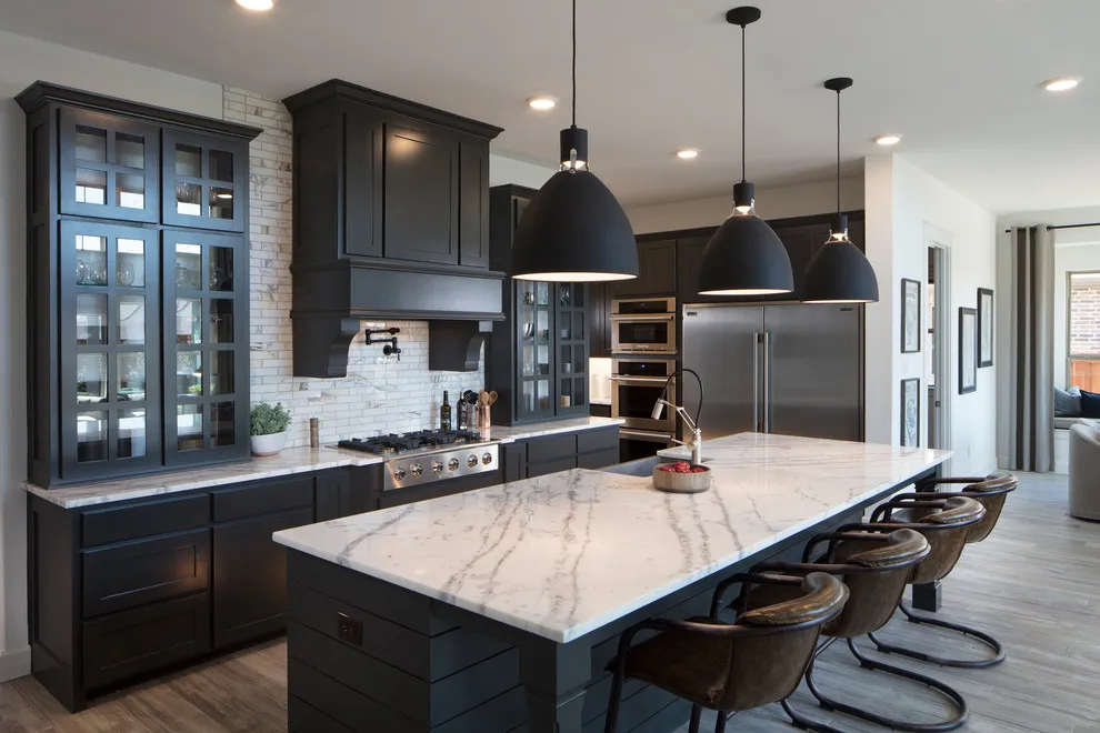Dark paneled cabinets surround a pale island worktop beneath black pendants