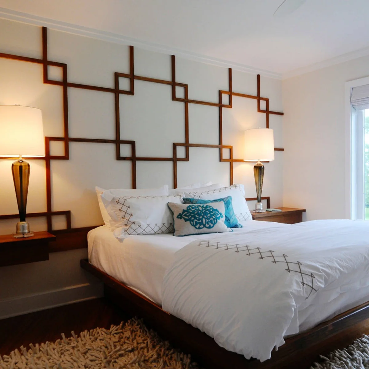 A thick cream rug is visible around a dark wood platform bed beneath a geometric wood wall treatment.