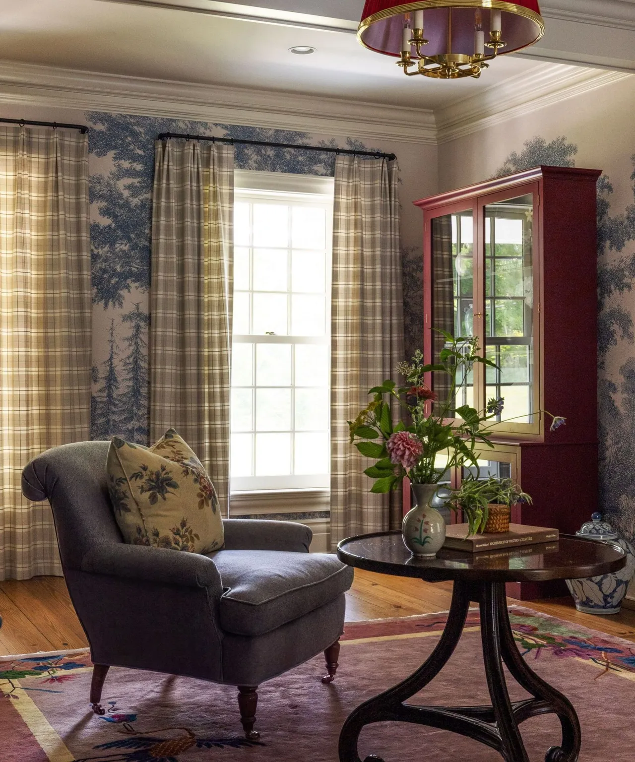A dark armchair sits beside a round table near layered curtains.
