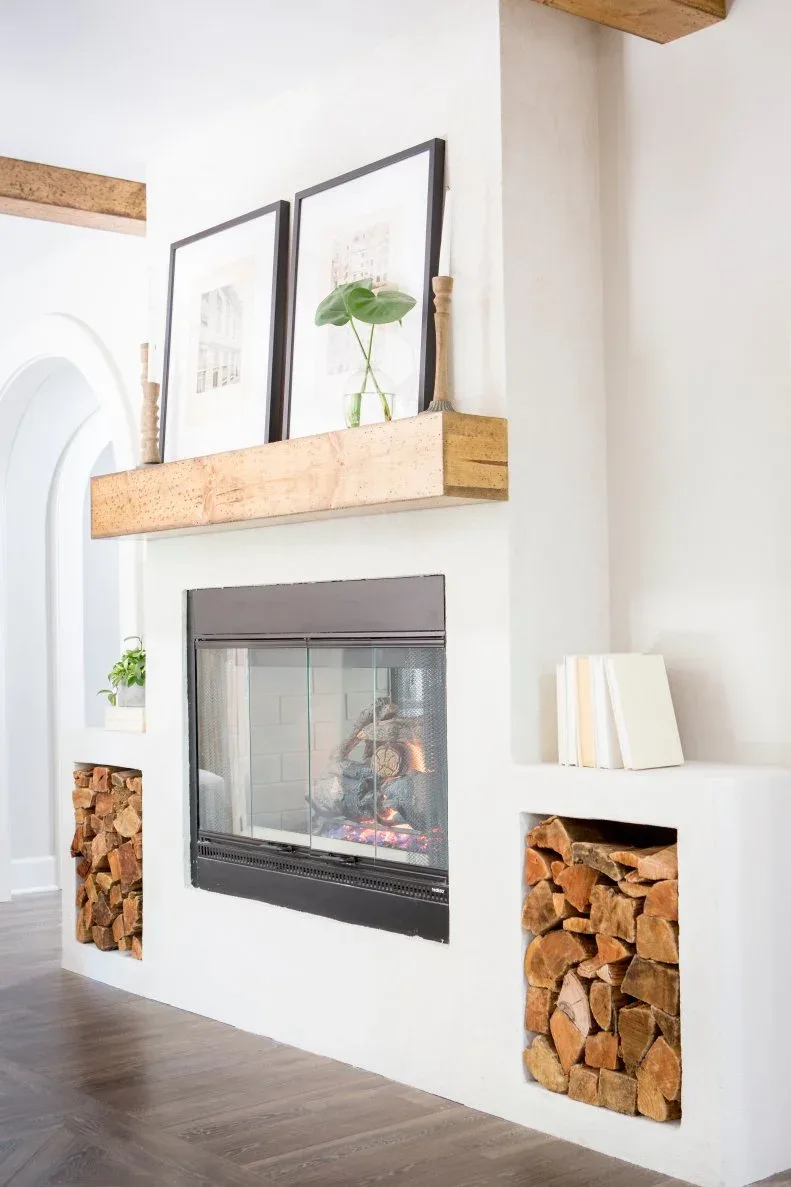A rough timber mantel sits above a glass-front fireplace with recessed log storage on both sides.