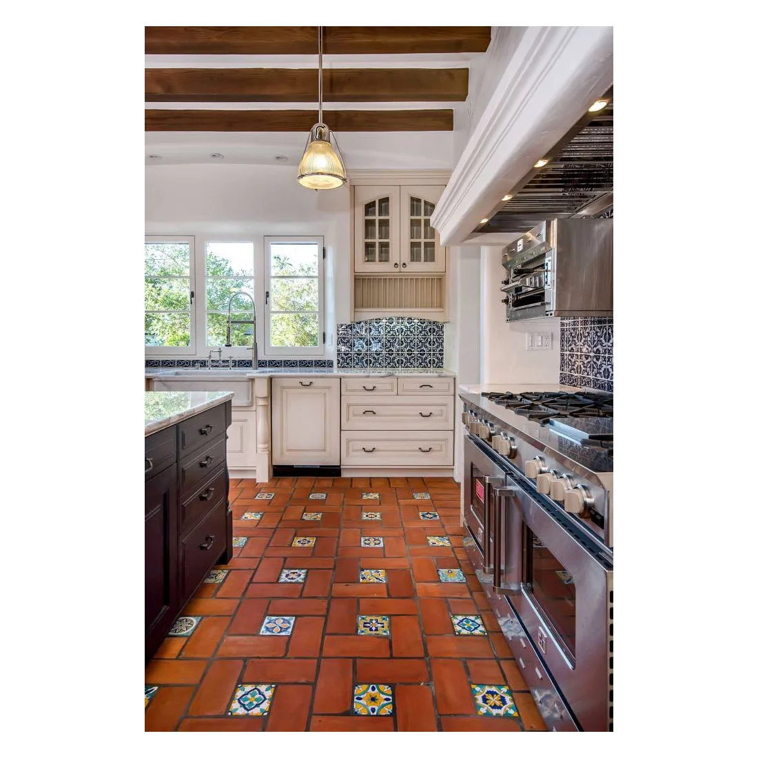 Small patterned inserts interrupt warm terracotta floor tiles beneath white cabinets and dark blue backsplash tiles.