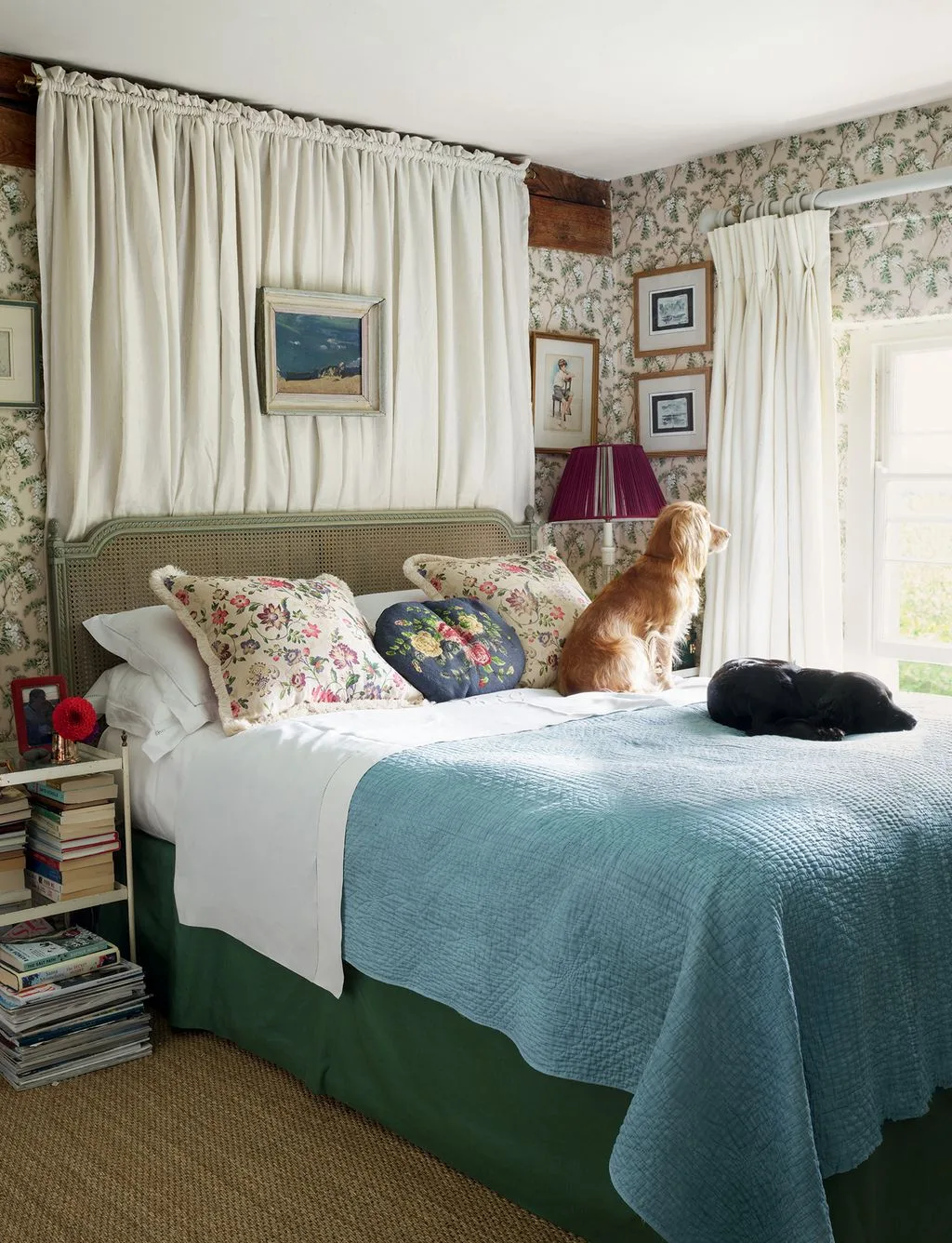 Bedroom with green woven-panel headboard, cream gathered wall fabric, floral cushions, blue cover, green bed skirt and framed pictures
