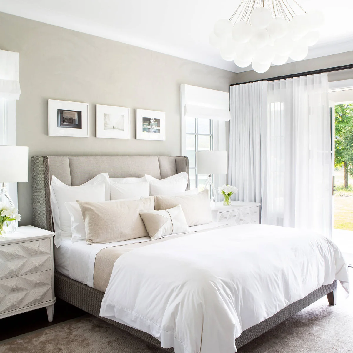 Three small white-framed pictures in a row above a pale winged headboard beside white curtains.