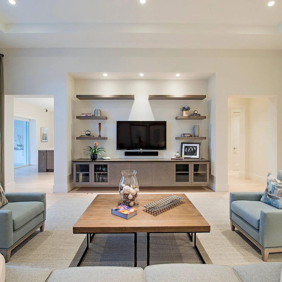 TV over a long wood-toned cabinet with staggered floating shelves inside a wall recess