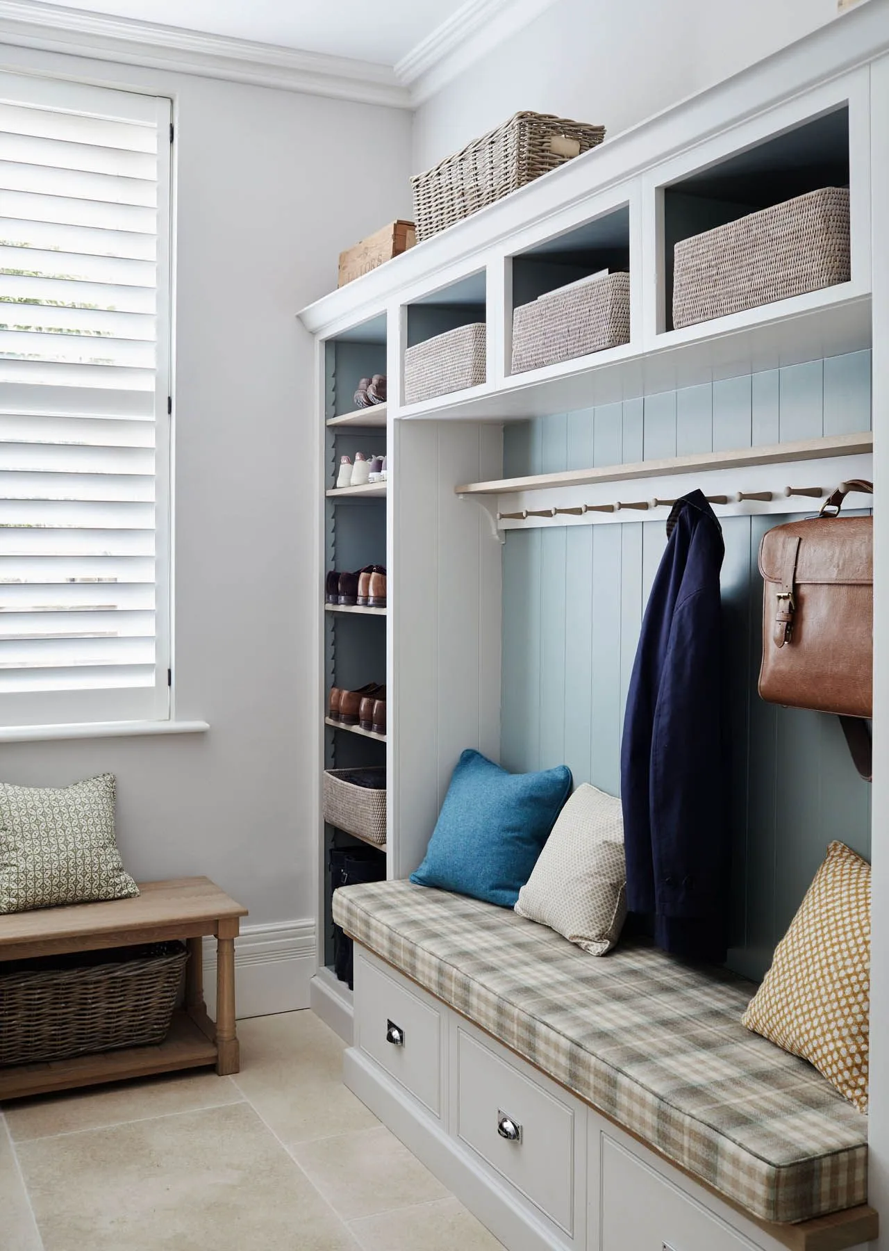 Pale blue entry storage with a checked bench cushion, upper baskets, a side shoe shelf and coats on a rail