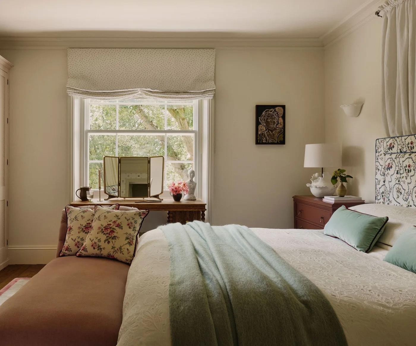 Cream bedroom walls around a floral headboard, pale green bedding and a wooden dressing table.