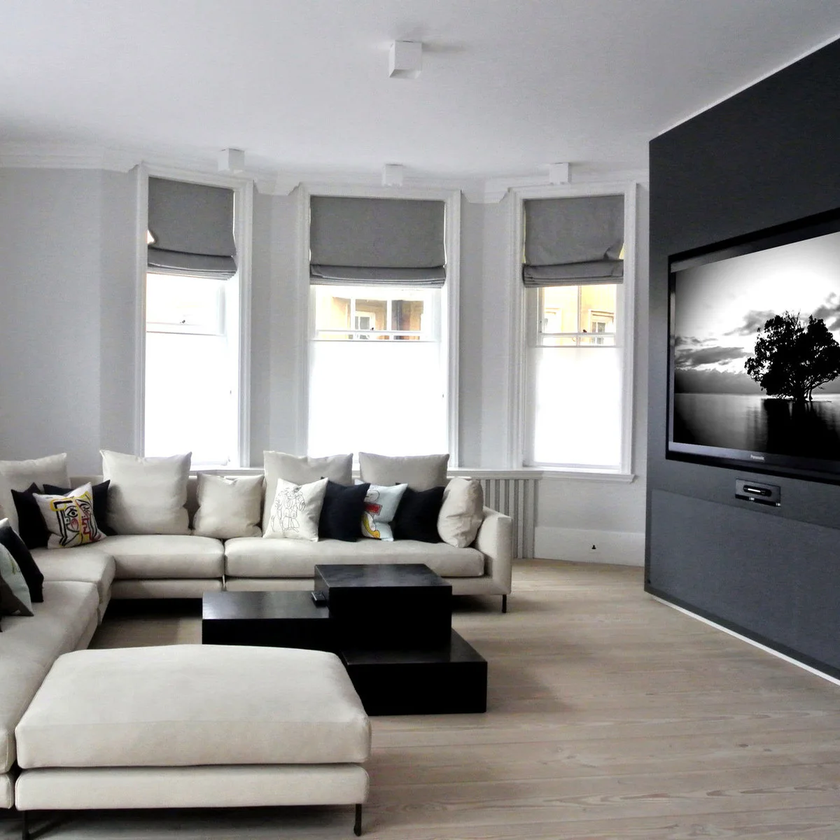 Pale corner sofa facing a dark media wall and small black stepped coffee tables