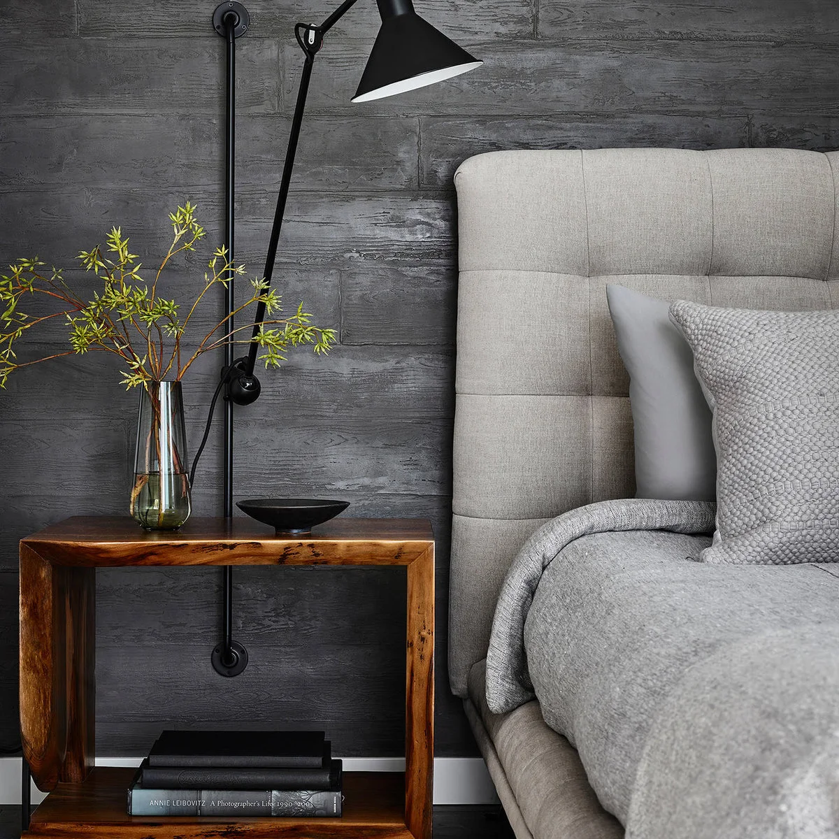 Open rectangular wooden bedside table against a textured gray wall with black reading light