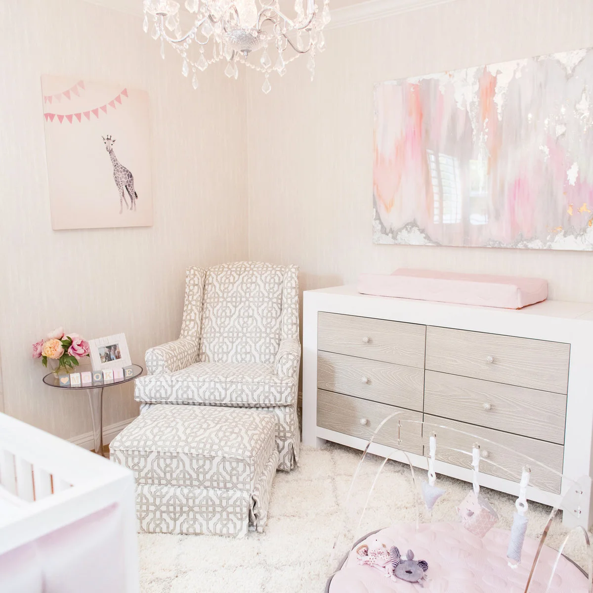 Nursery corner with a patterned armchair and footstool beside a white six-drawer changing dresser