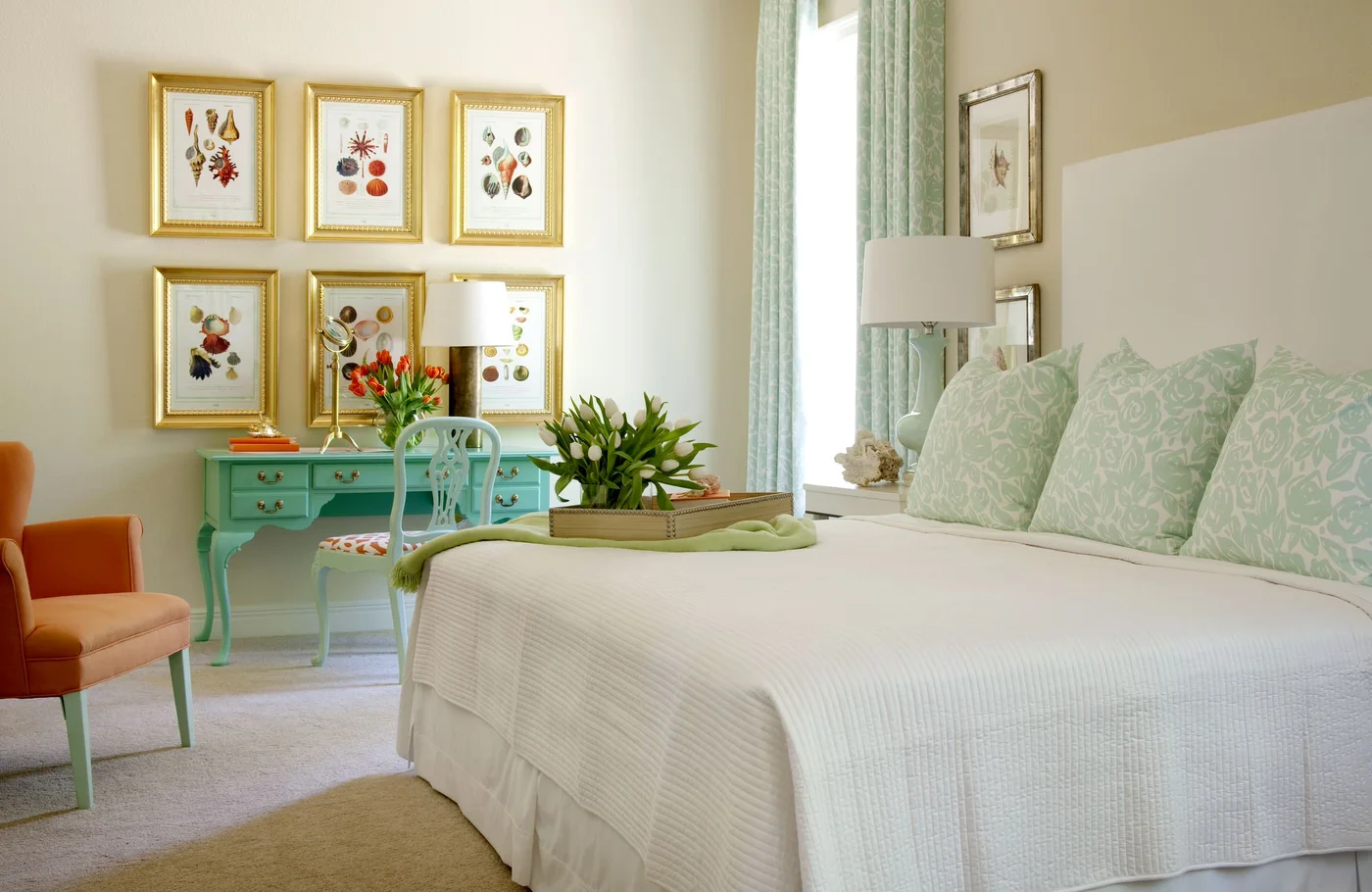 Bedroom with a turquoise writing desk, pale green patterned pillows and curtains, and an orange chair