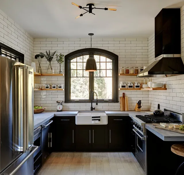 Black lower cabinets sit around an arched window beneath pale tile and timber shelves.