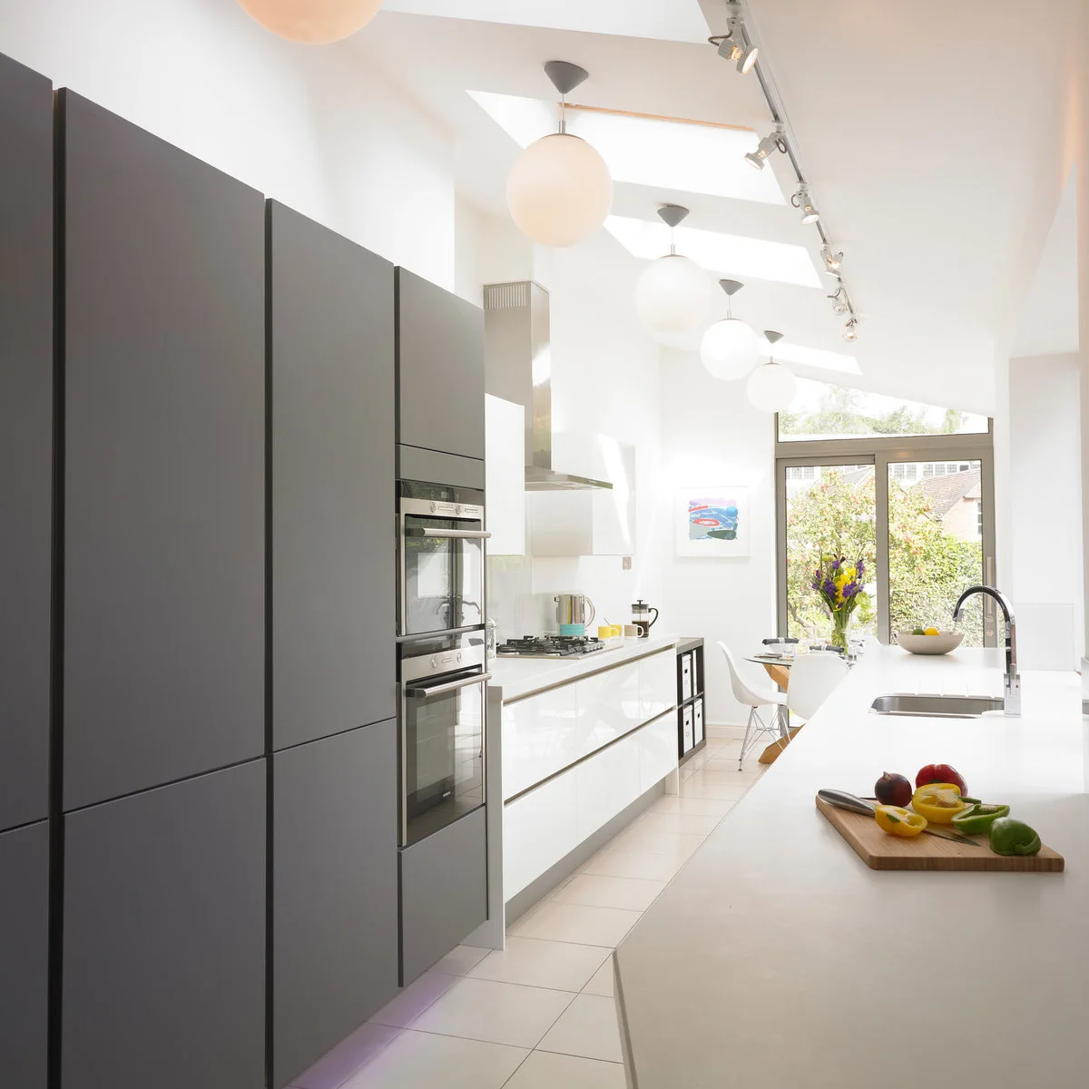 Terraced-house galley kitchen with gray tall storage, white lower cabinets and a small table by glazed doors