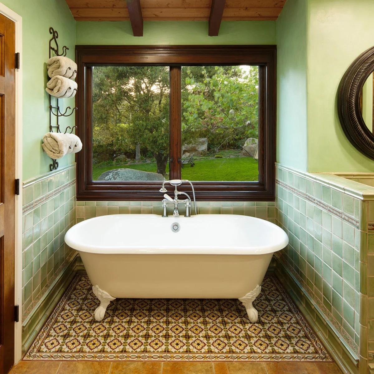 Bathroom with green square wall tiles, a multicolored patterned floor and a white clawfoot tub